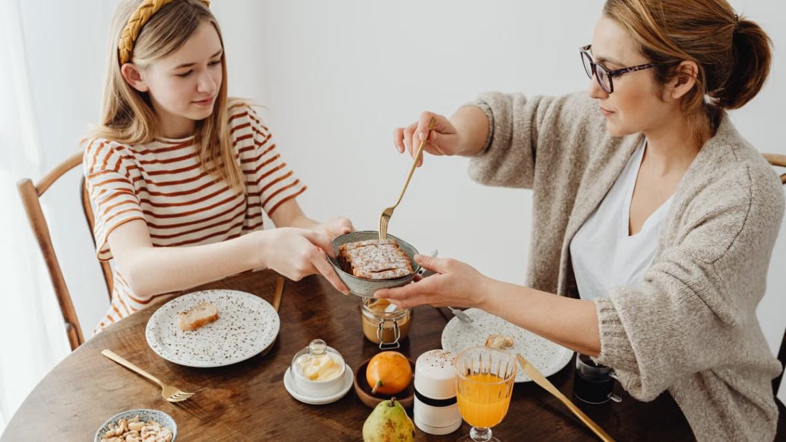 A mother and daughter enjoying a cozy breakfast with toast and juice at the dining table.